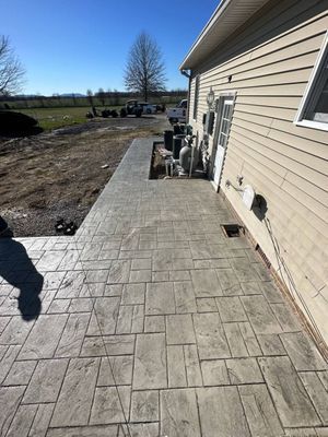 A newly installed stamped concrete patio with a rectangular stone pattern alongside the side of a beige-sided house.