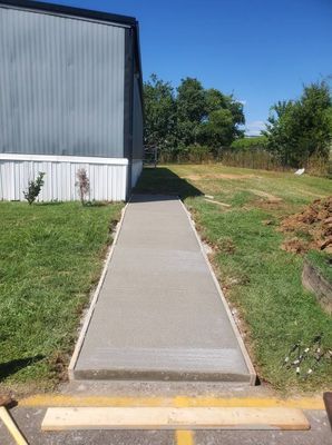 A straight concrete sidewalk leads toward the side of a metal-sided building on a sunny day.