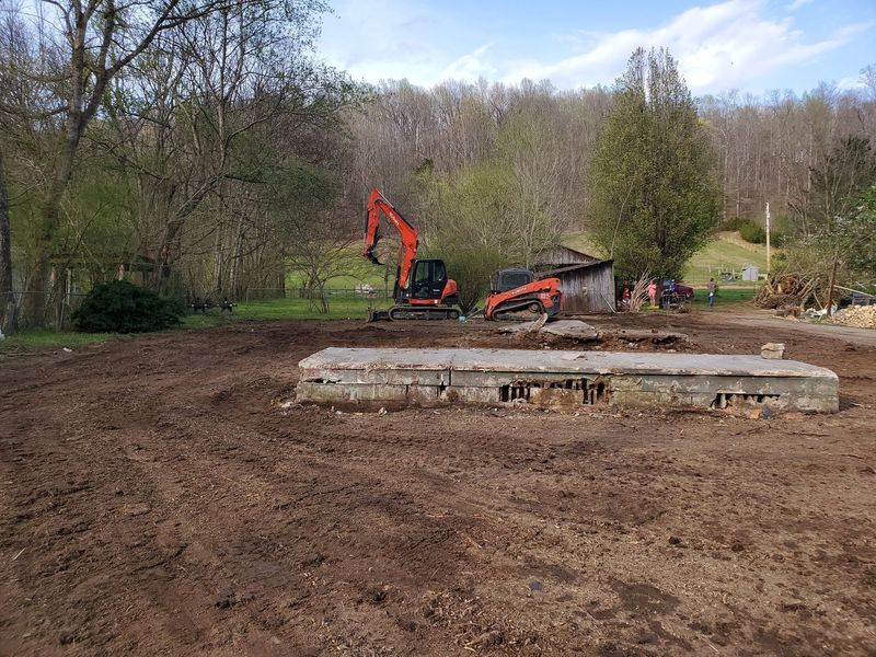 An orange excavator and skid-steer sit on a muddy plot of land behind a concrete building foundation.