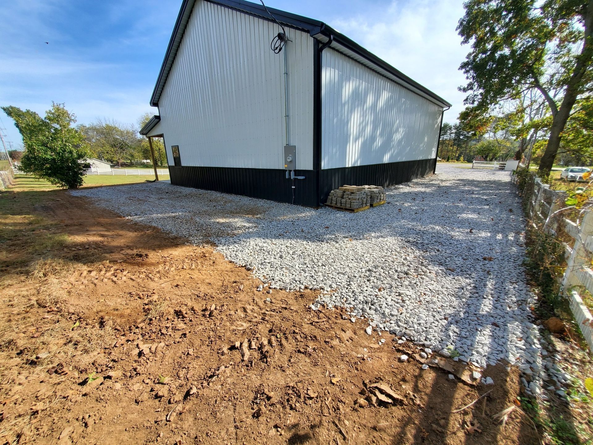 White building with a black base, surrounded by gravel and bare earth under a bright blue sky.
