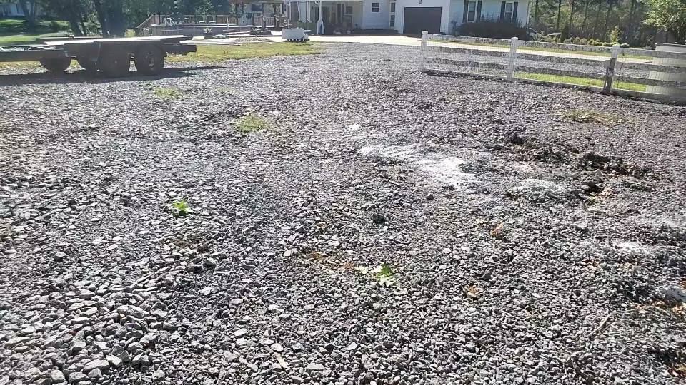 A gravel driveway leads toward a house with a white fence on a sunny day.