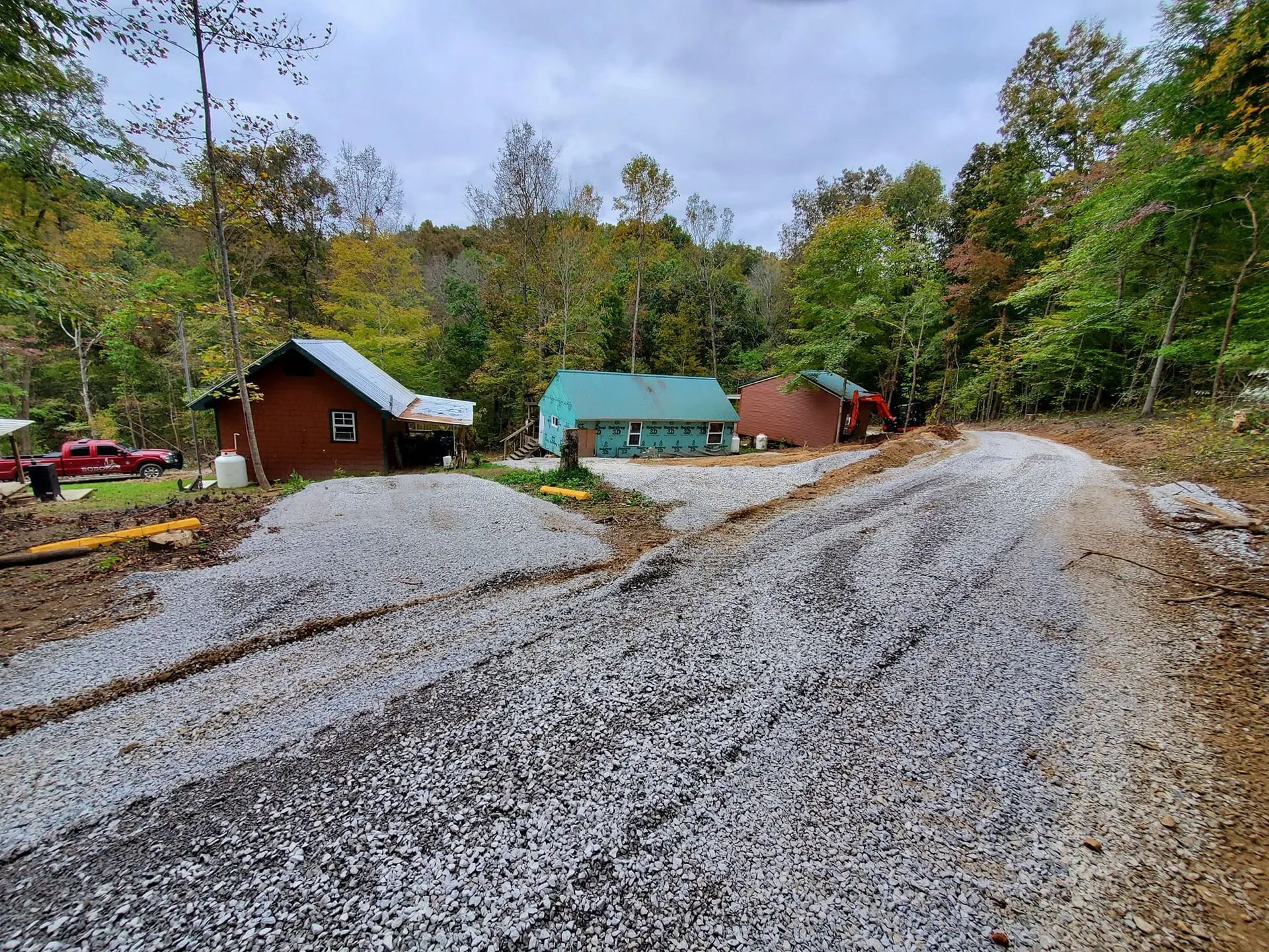 Gravel path leading to three buildings set against a backdrop of green and autumnal trees under a cloudy sky.