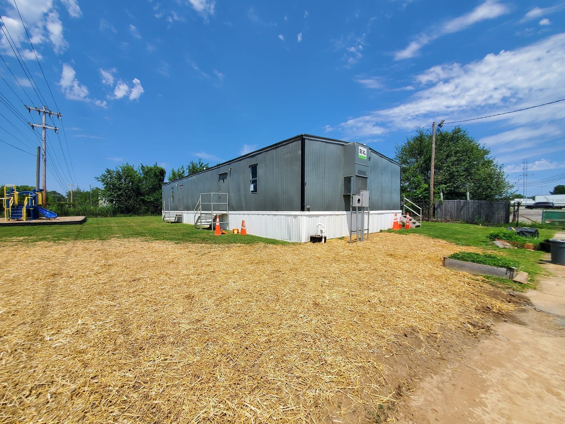 A rectangular, grey metal modular building on a white base, situated in an outdoor area covered with wood chips.