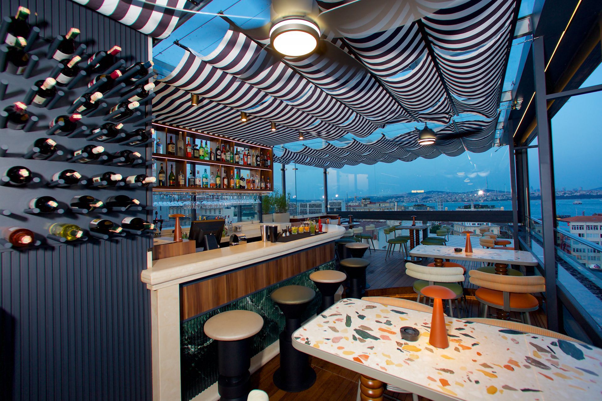 A restaurant with tables and chairs and a bar with bottles of wine on the wall.