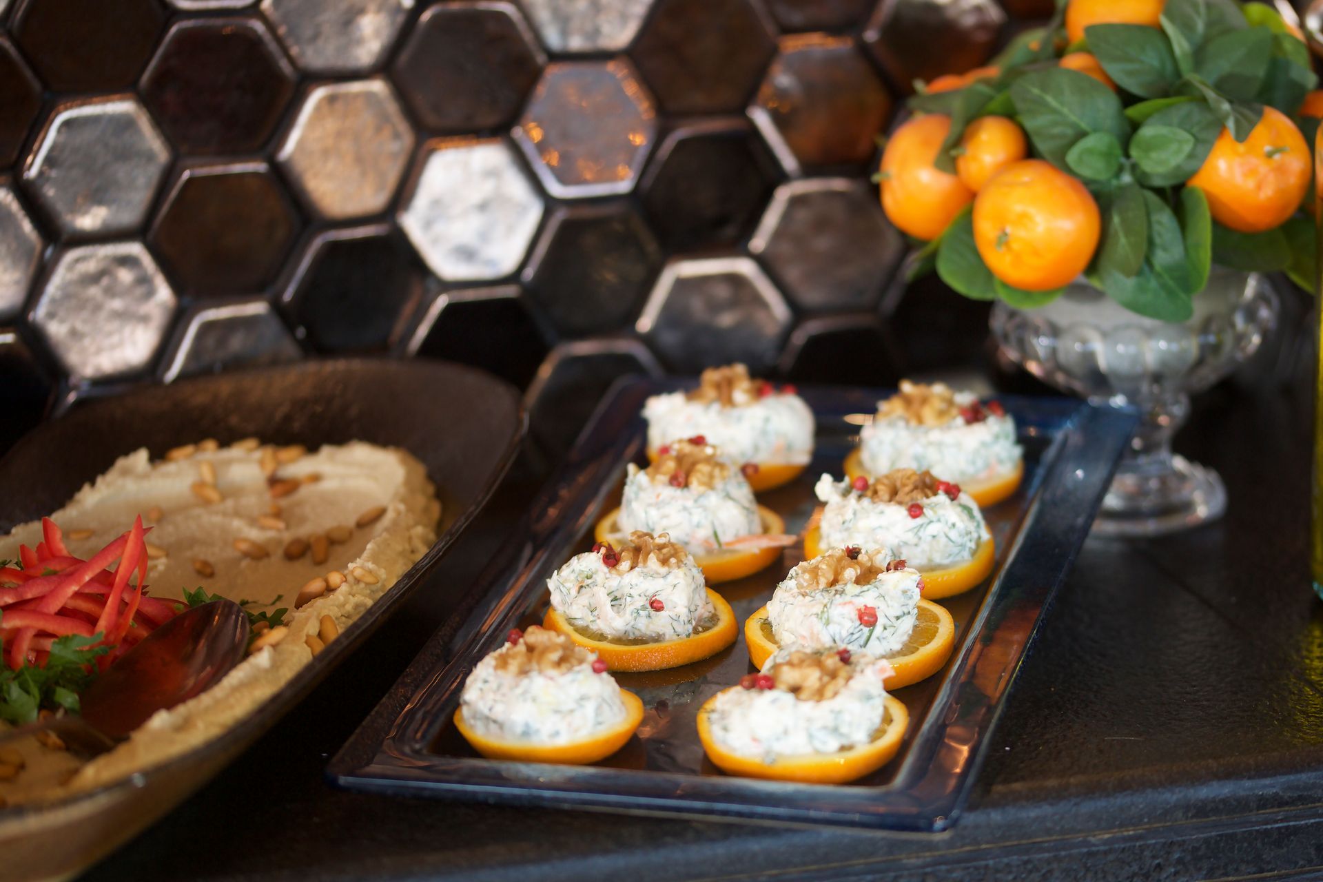A tray of food is sitting on a table next to a vase of oranges.