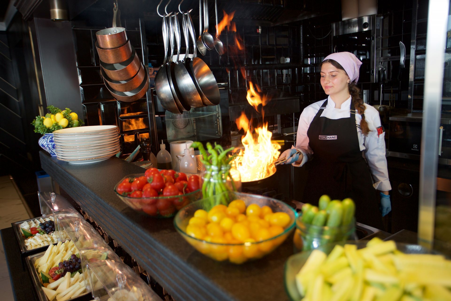 A woman is cooking food in a kitchen with flames coming out of a pan.