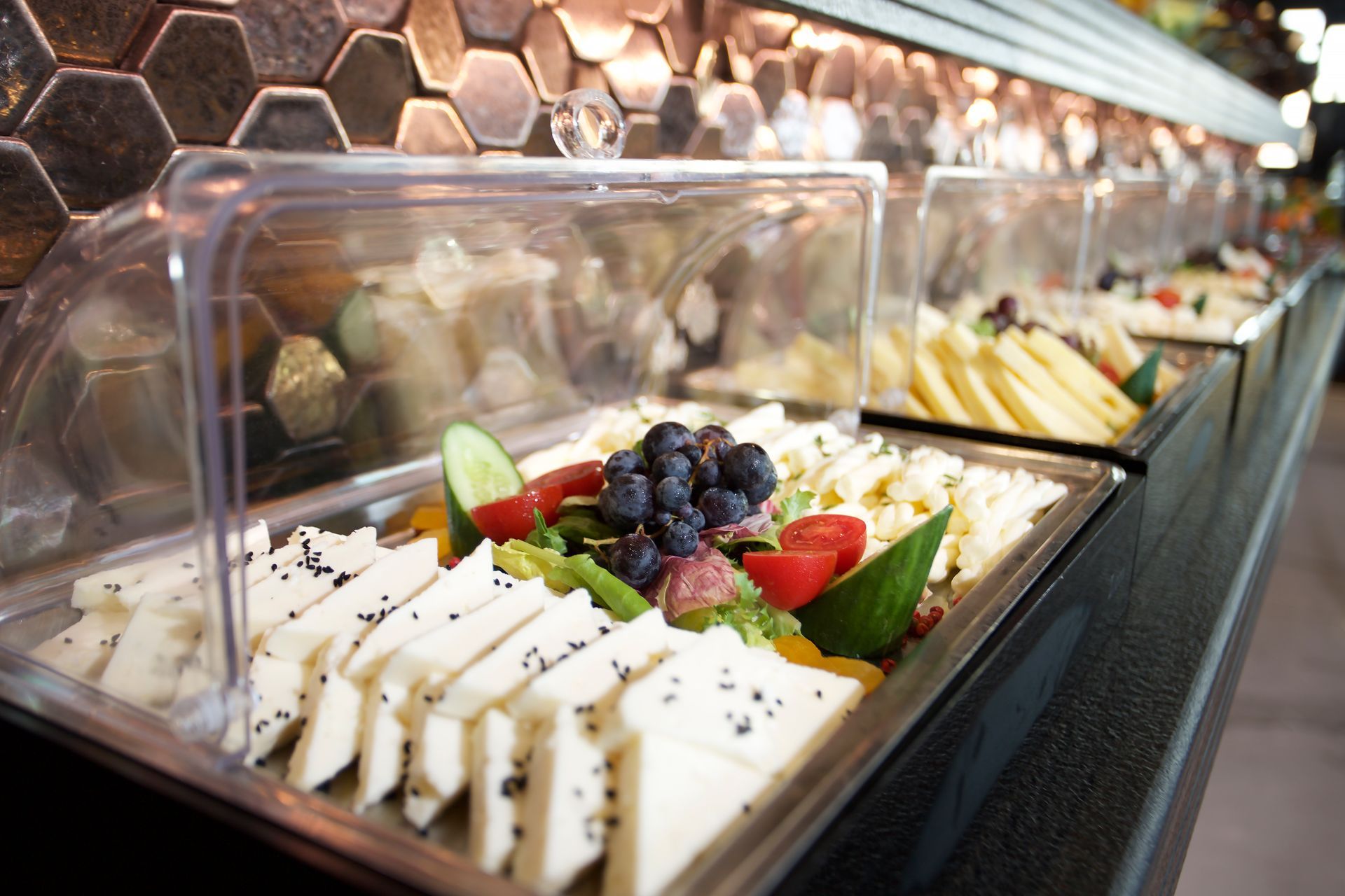 A buffet filled with a variety of food including cheese , fruit and vegetables.