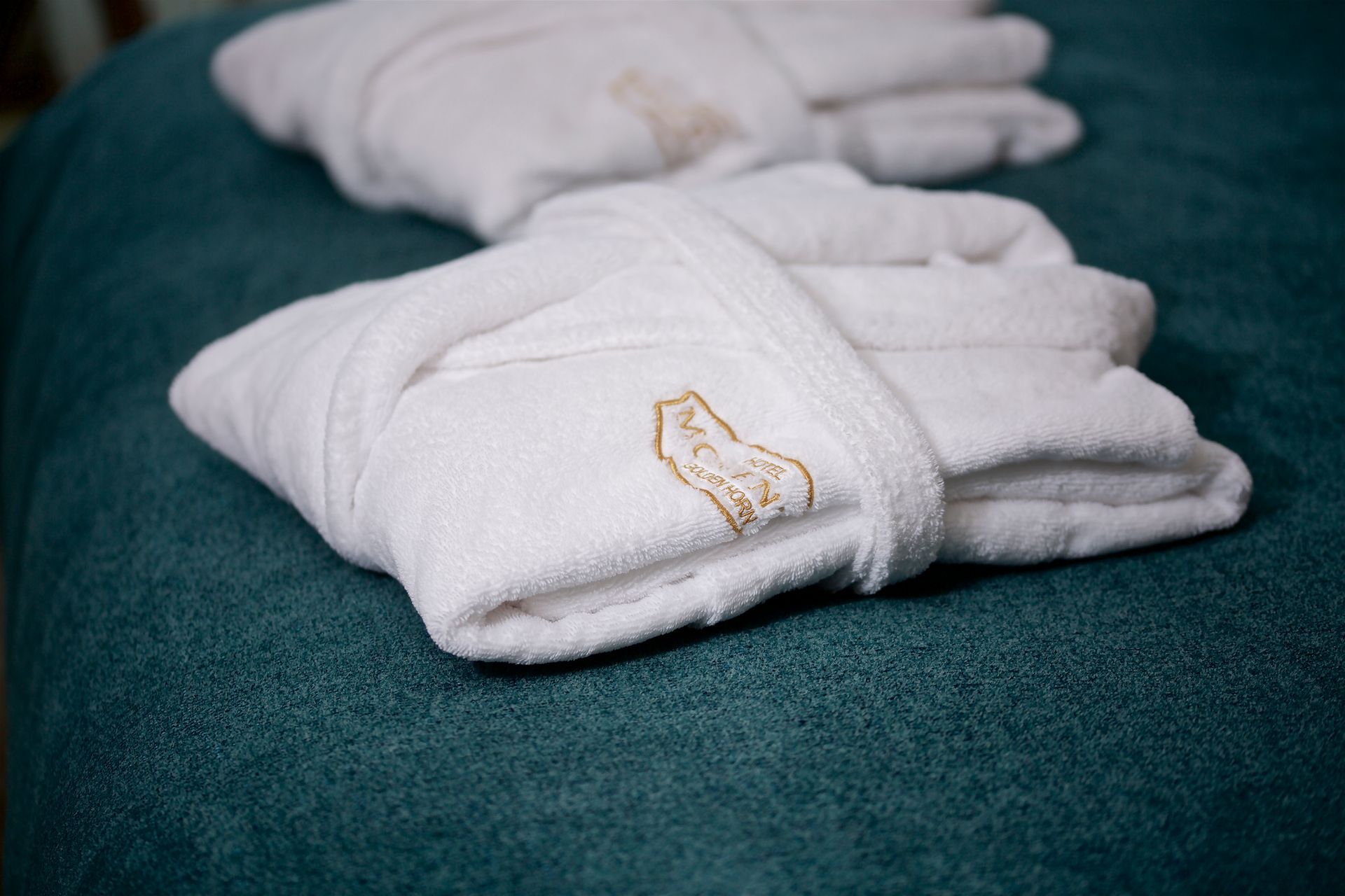 Three white bathrobes are stacked on top of each other on a bed.