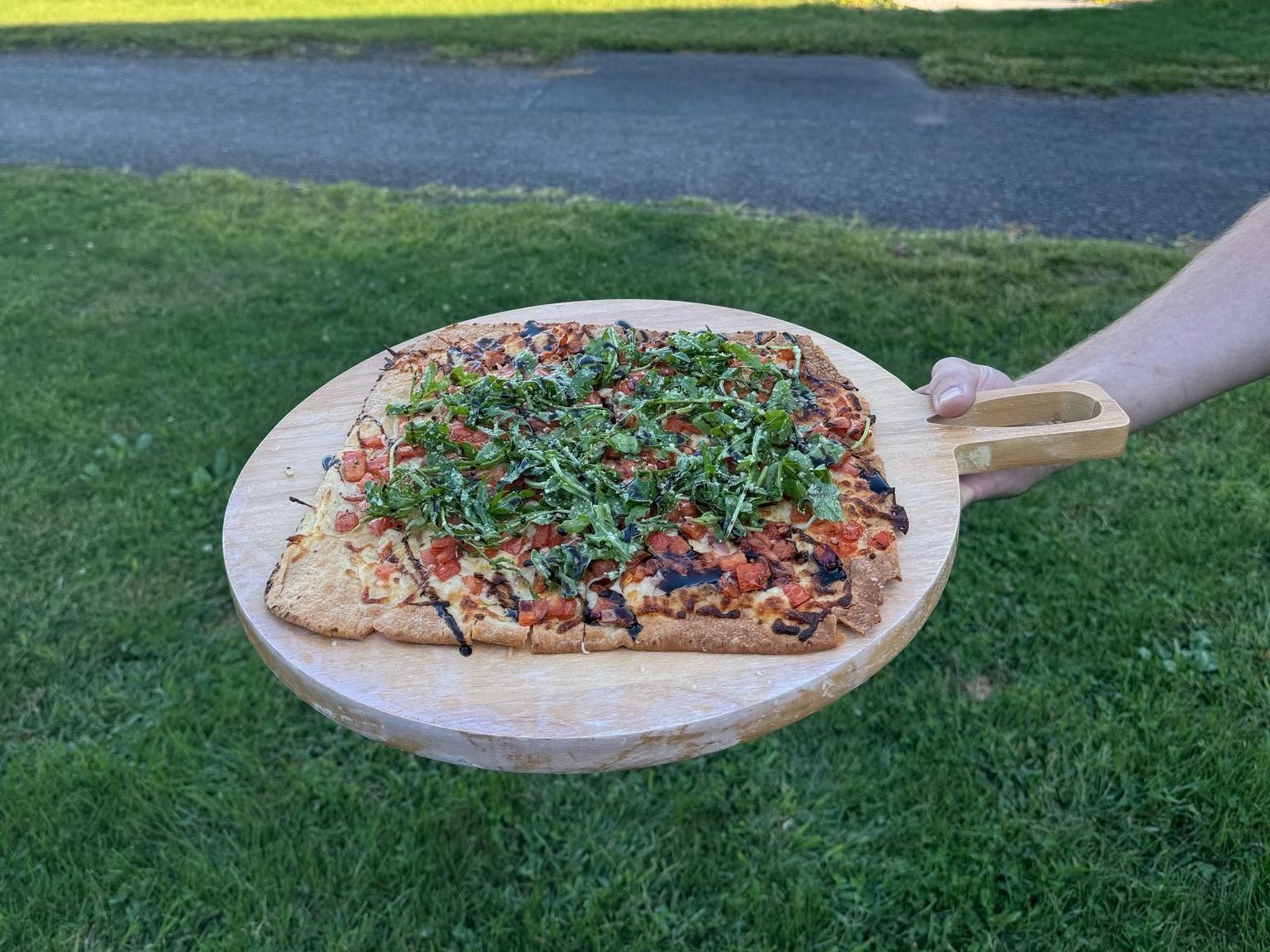 A person is holding a pizza on a wooden cutting board.