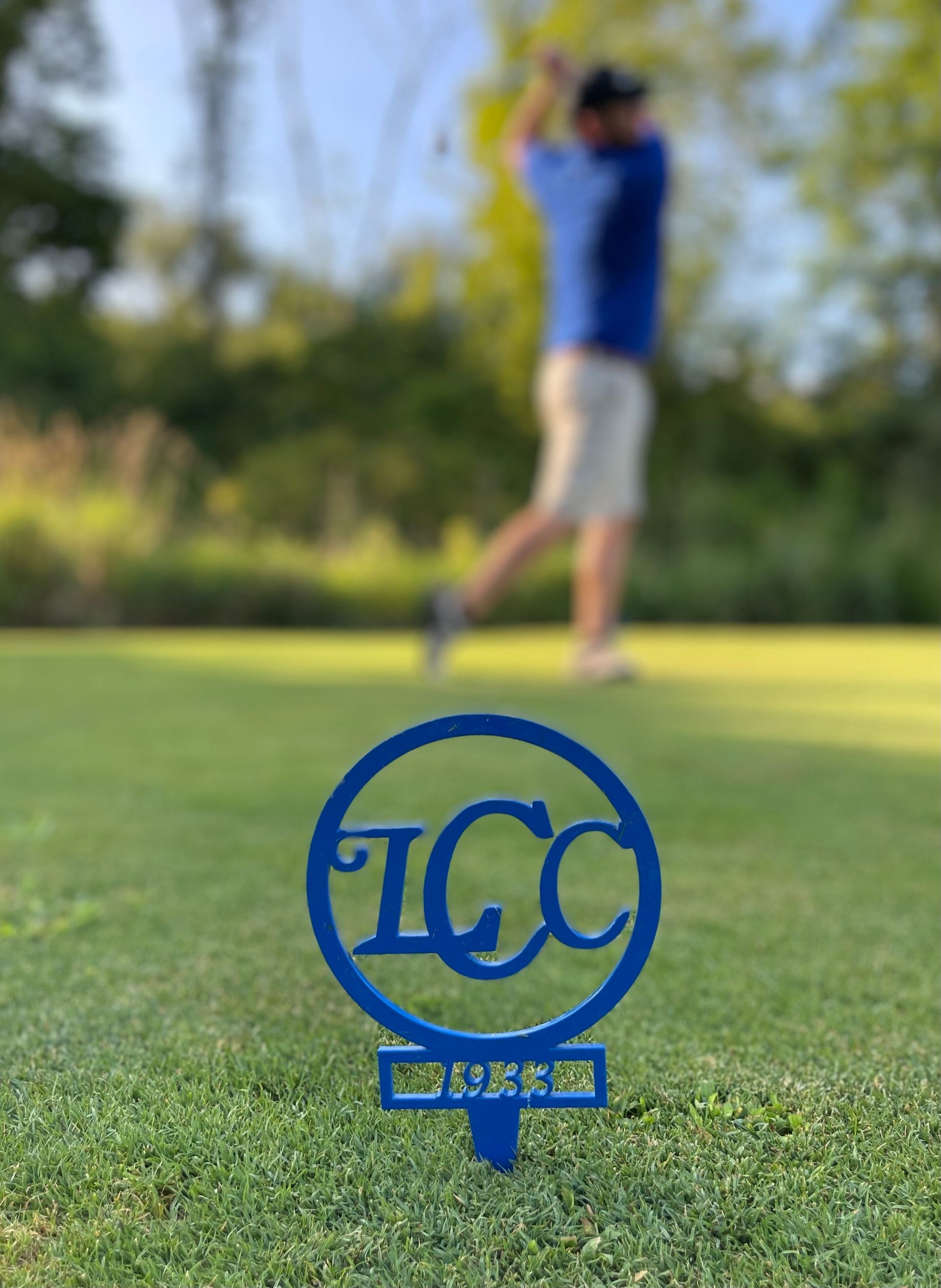 A man in a blue shirt is swinging a golf club on a golf course.