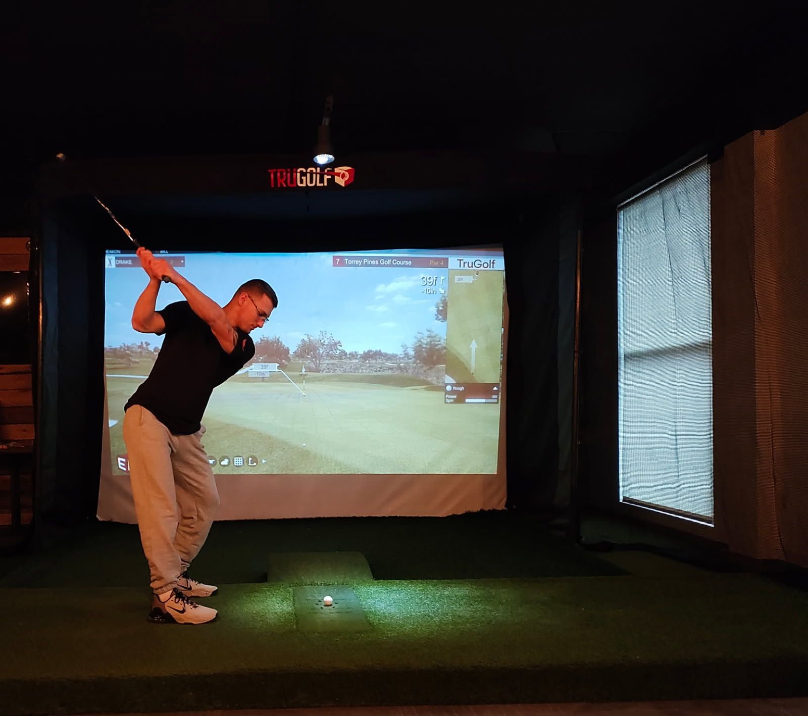 A man is swinging a golf club in front of a screen that says golf