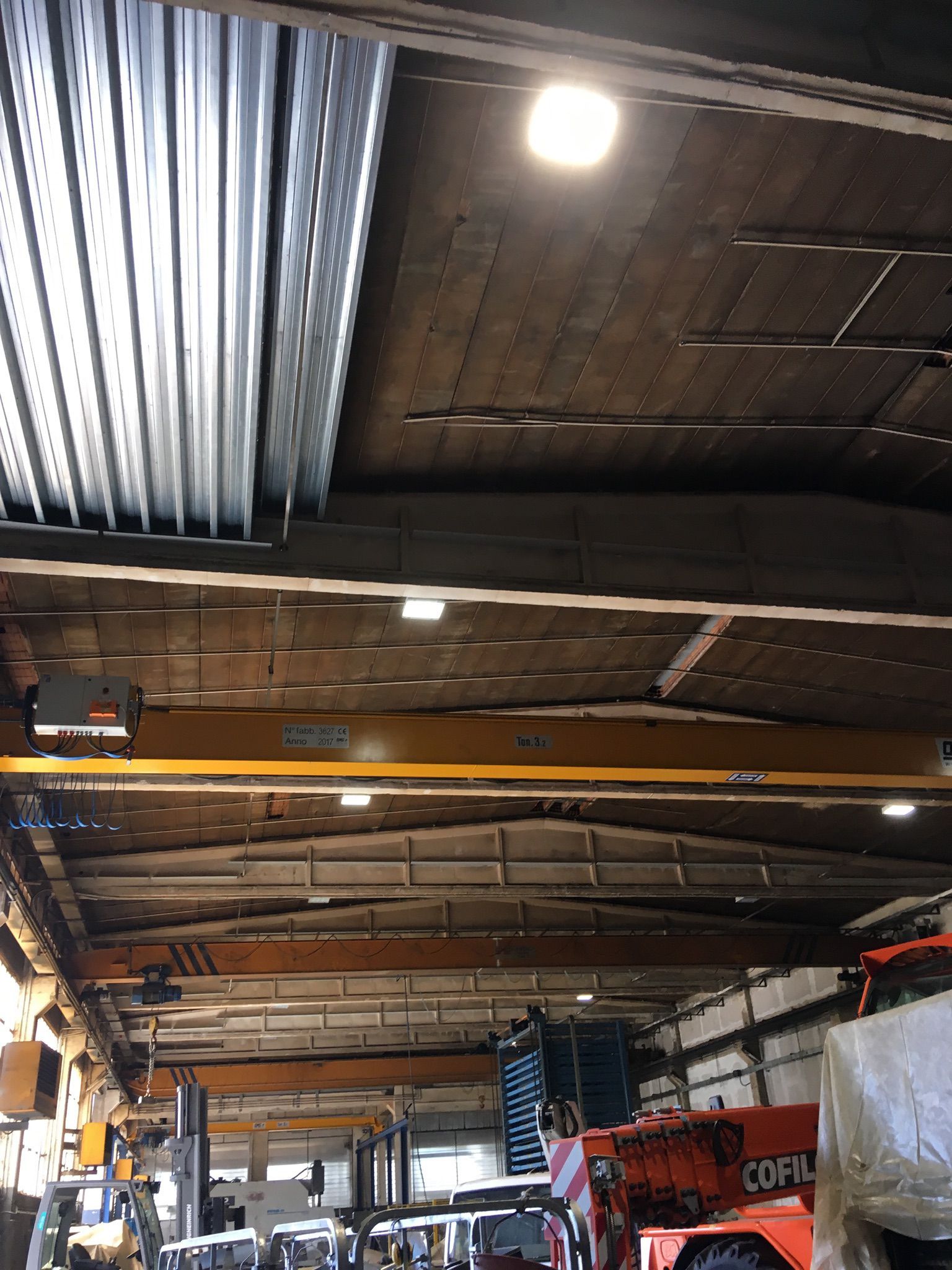 Interno del magazzino con gru a ponte, illuminazione e macchinari.