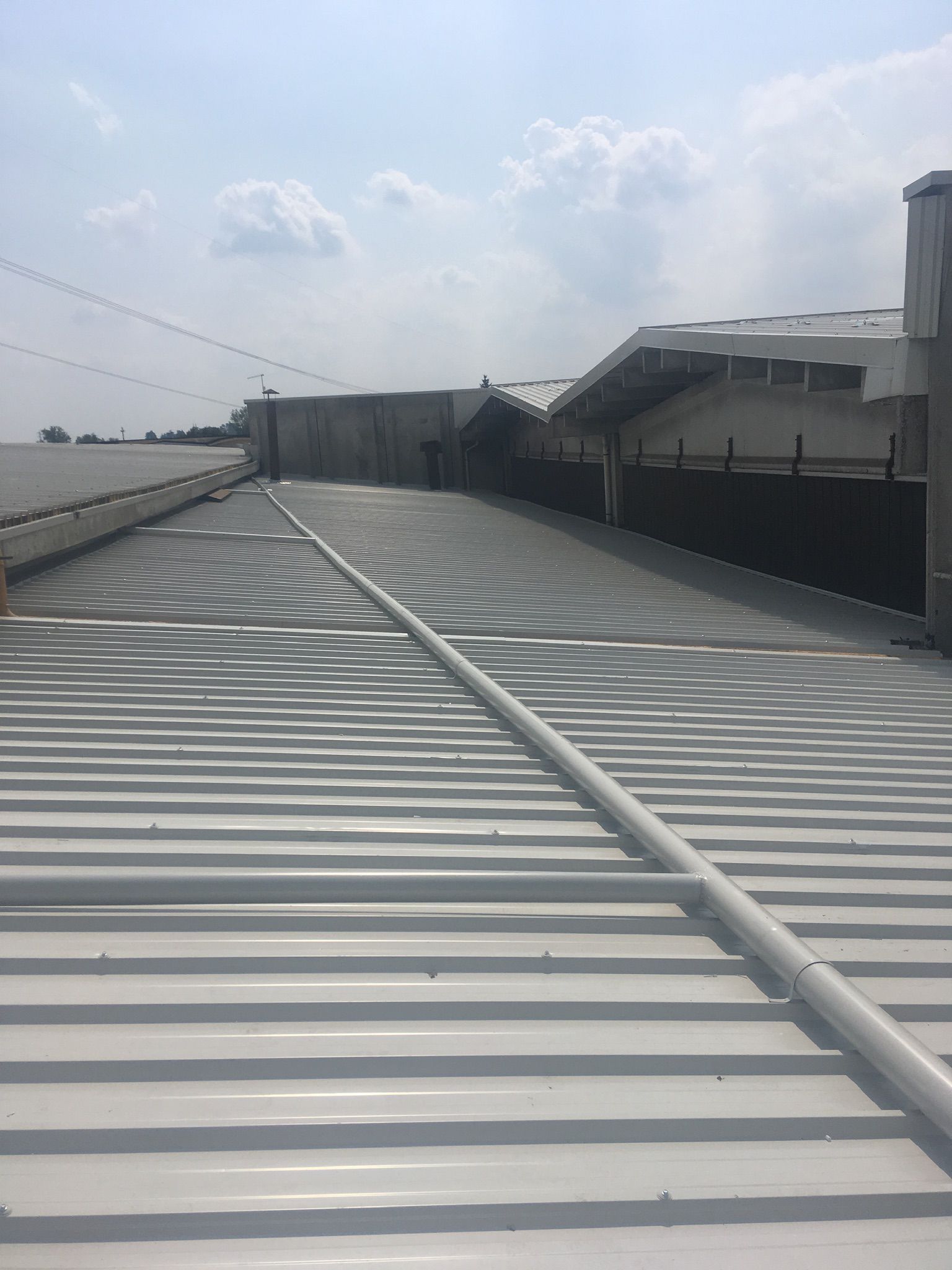 Tetto in lamiera ondulata bianca con pannelli solari, sotto un cielo azzurro.