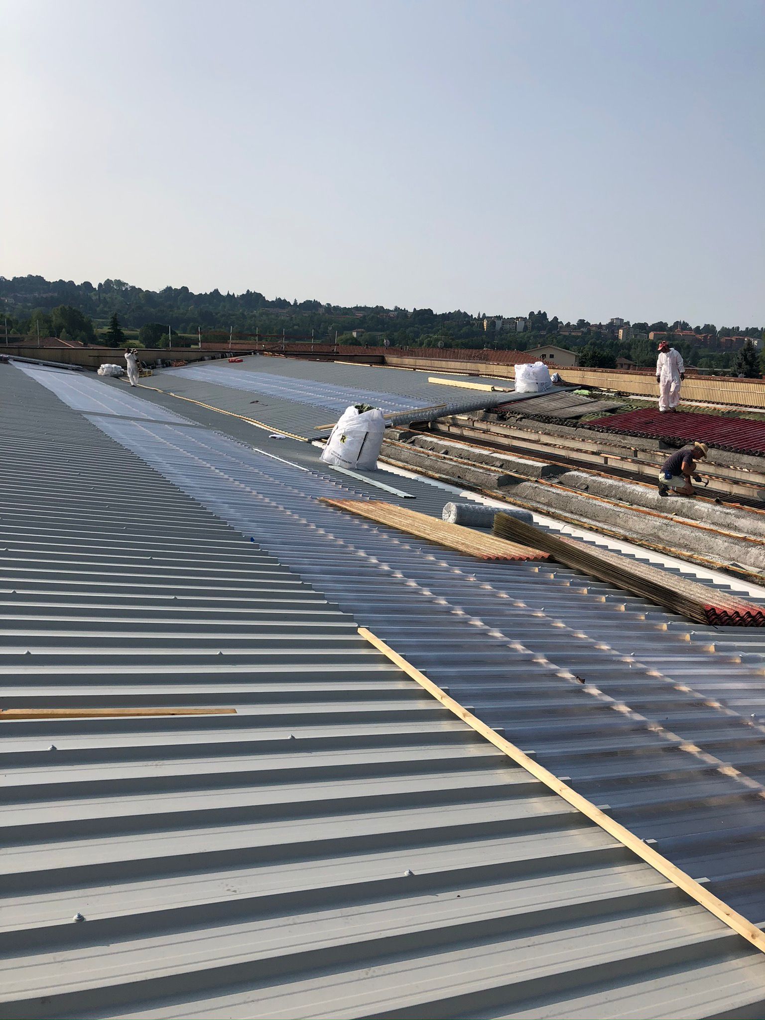 Un balcone con tetto in vetro e tegole in costruzione, attrezzi a vista, che si affaccia su un giardino.