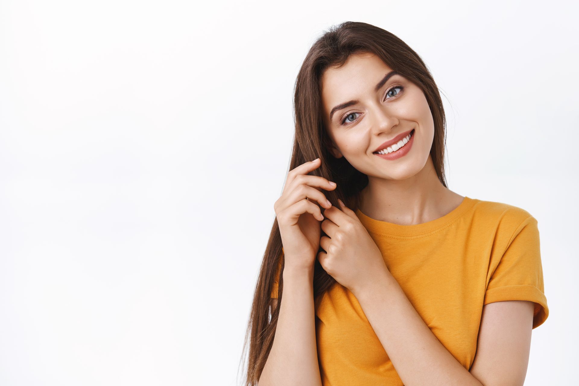 a woman in a yellow shirt is smiling and touching her hair .