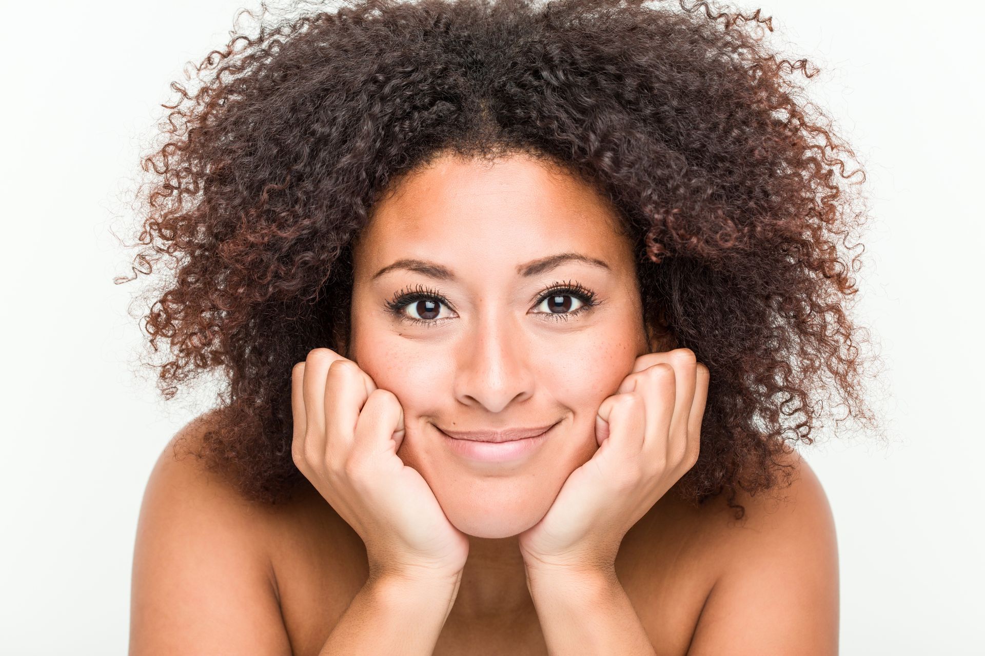 a woman with curly hair is smiling with her hands on her face .