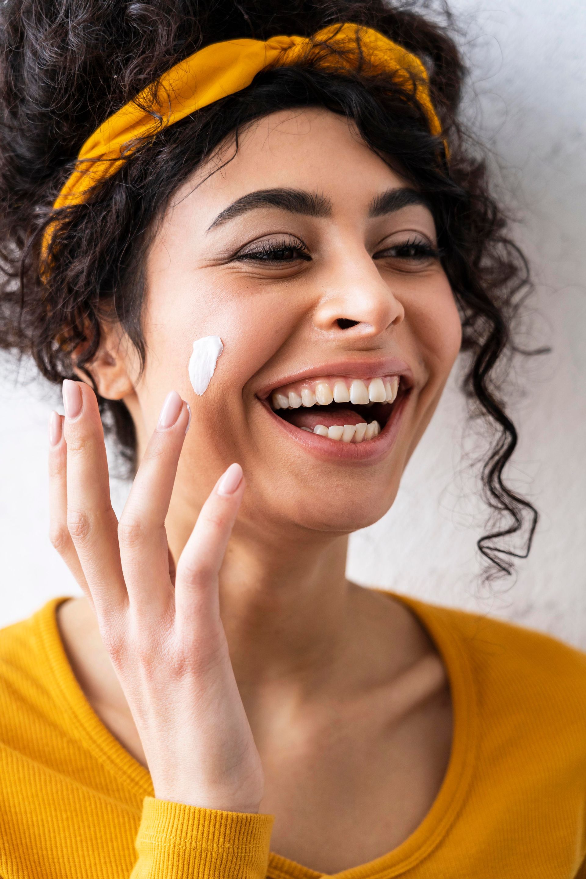 a woman is smiling while applying cream to her face .