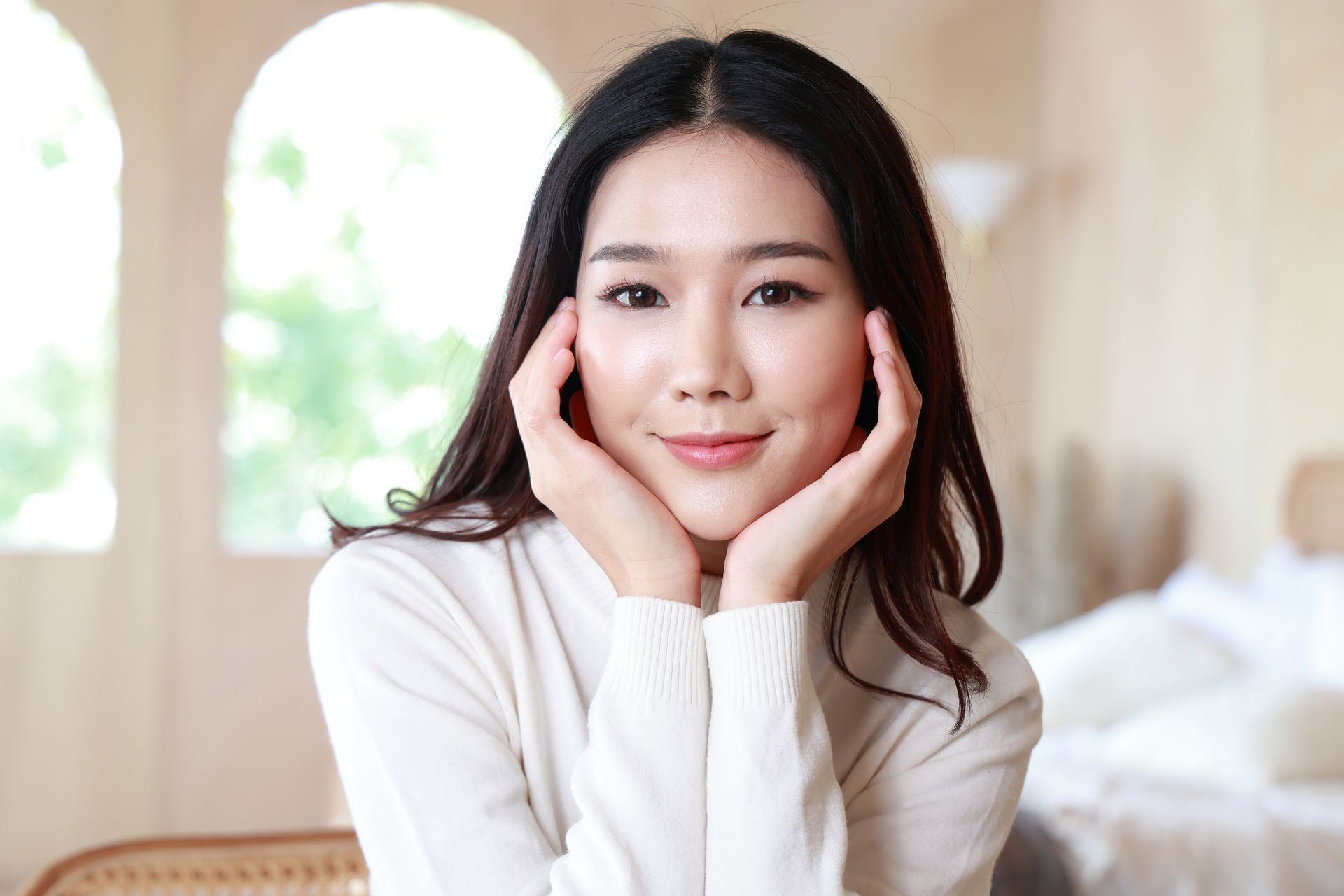 A woman in a white sweater is smiling with her hands on her face.