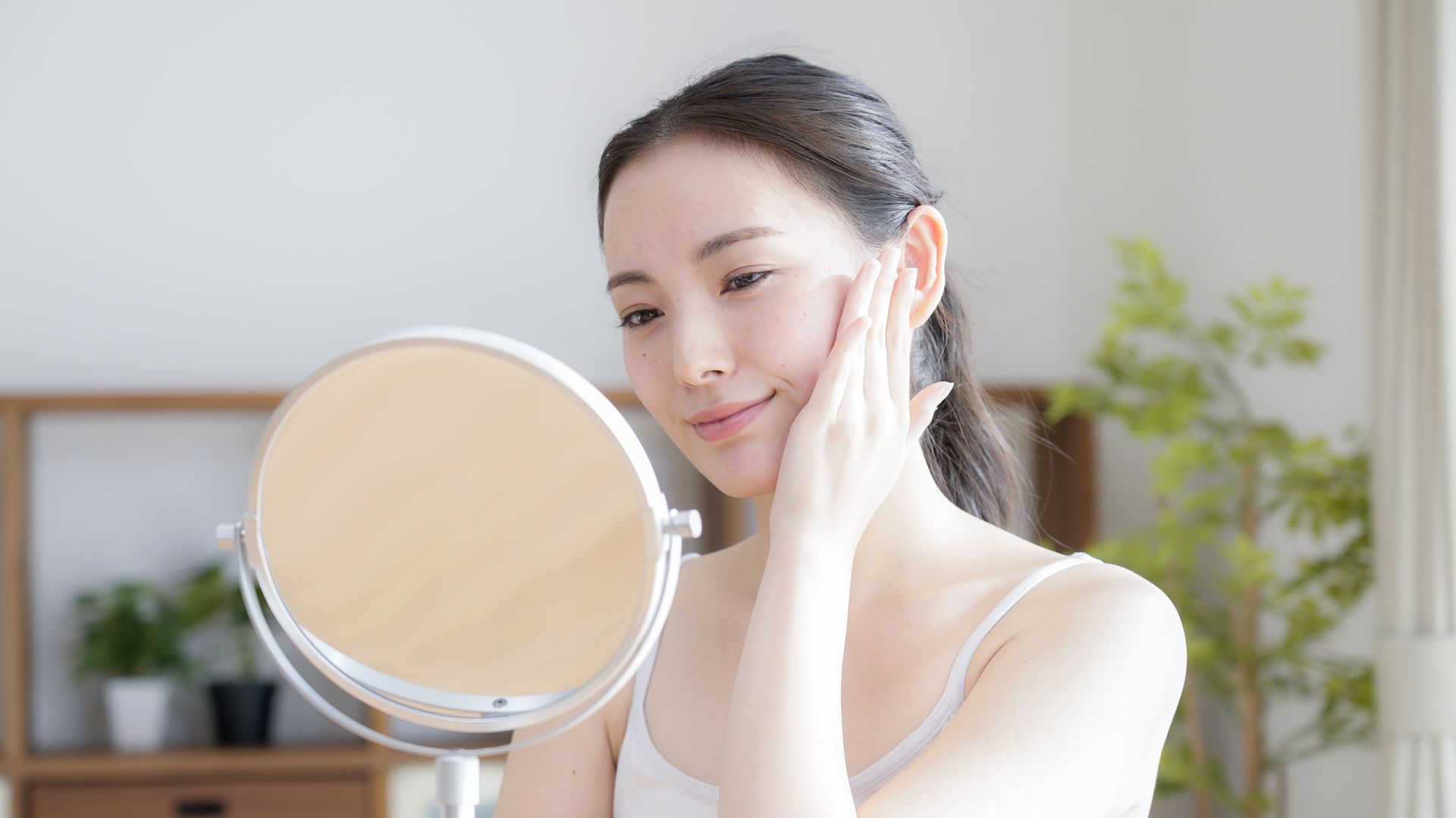 A woman is looking at her face in a mirror.