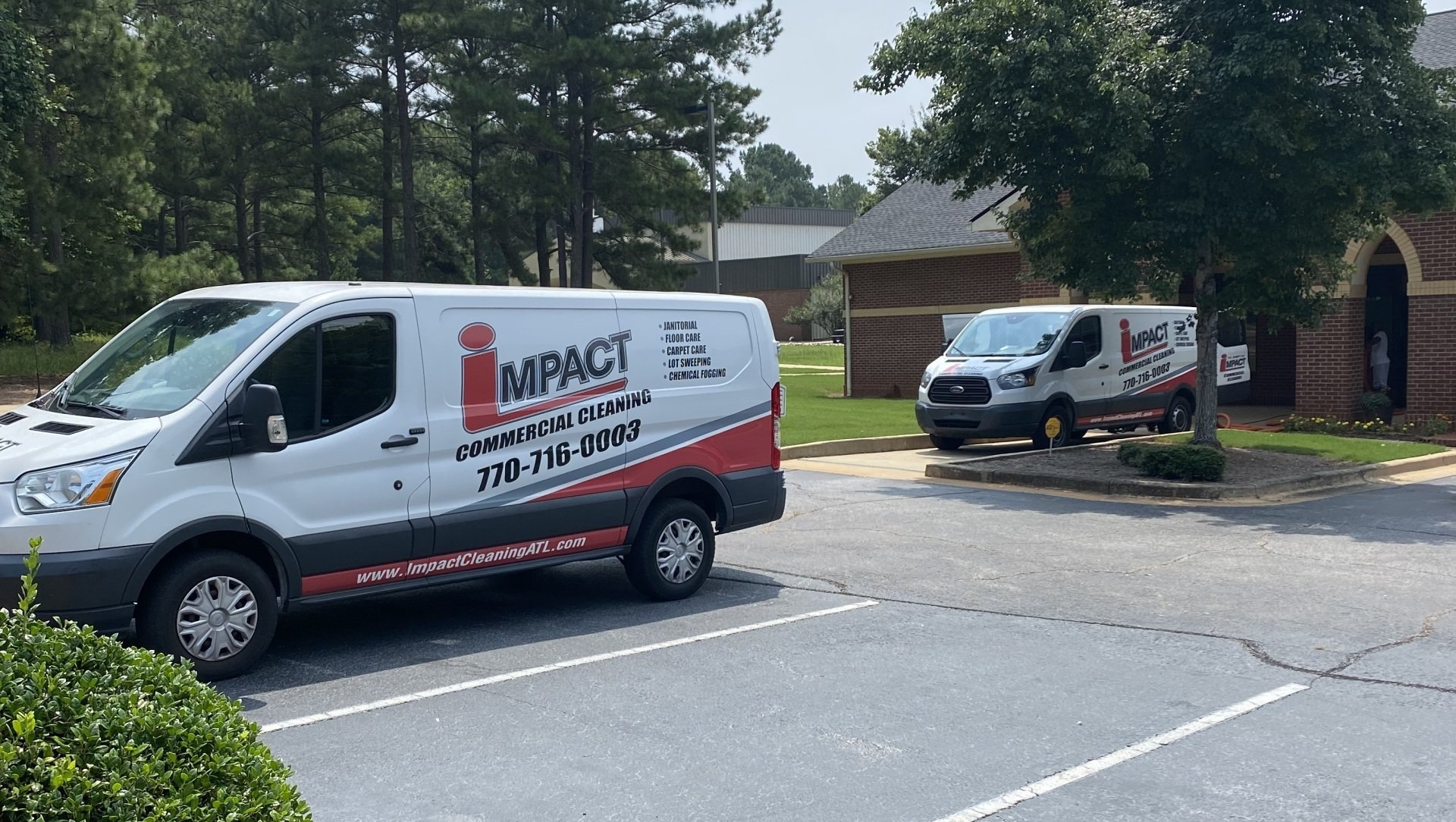 Two white Impact Communication vans parked outside a building.