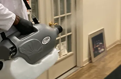 Person spraying disinfectant with a fogger near a doorway inside a building.