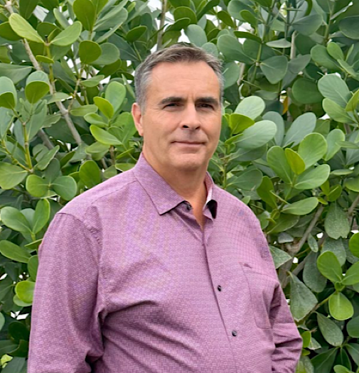 Woman in black turtleneck top, leaning on countertop, smiles.