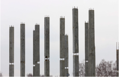 Rows of tall, gray concrete columns in construction site, set against a cloudy sky.