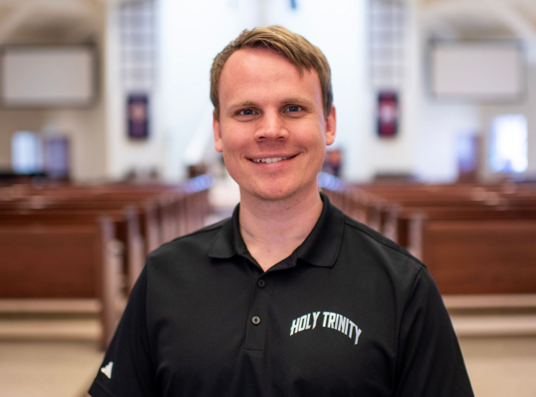 A man in a black shirt is smiling in front of a church.