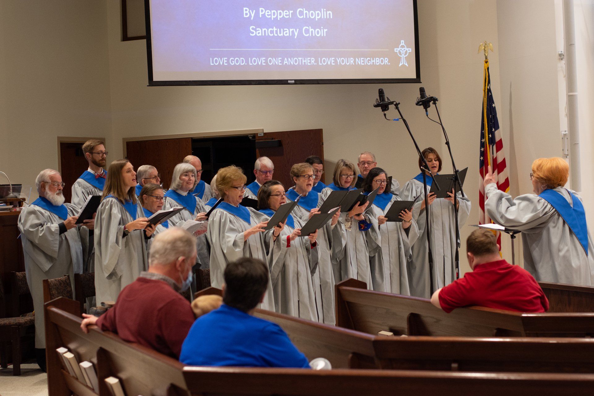 A choir is singing in a church with people sitting in the pews.