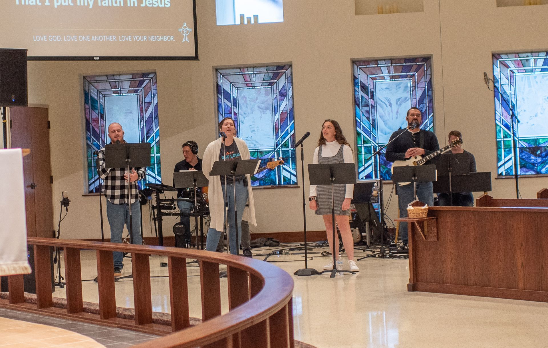 A group of people are singing in a church with stained glass windows.