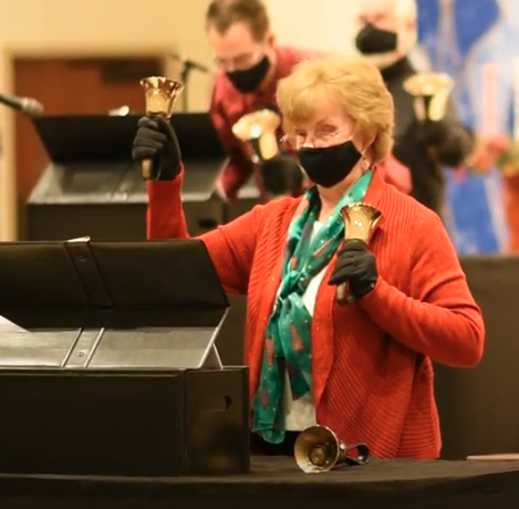 A woman wearing a mask is playing a bell