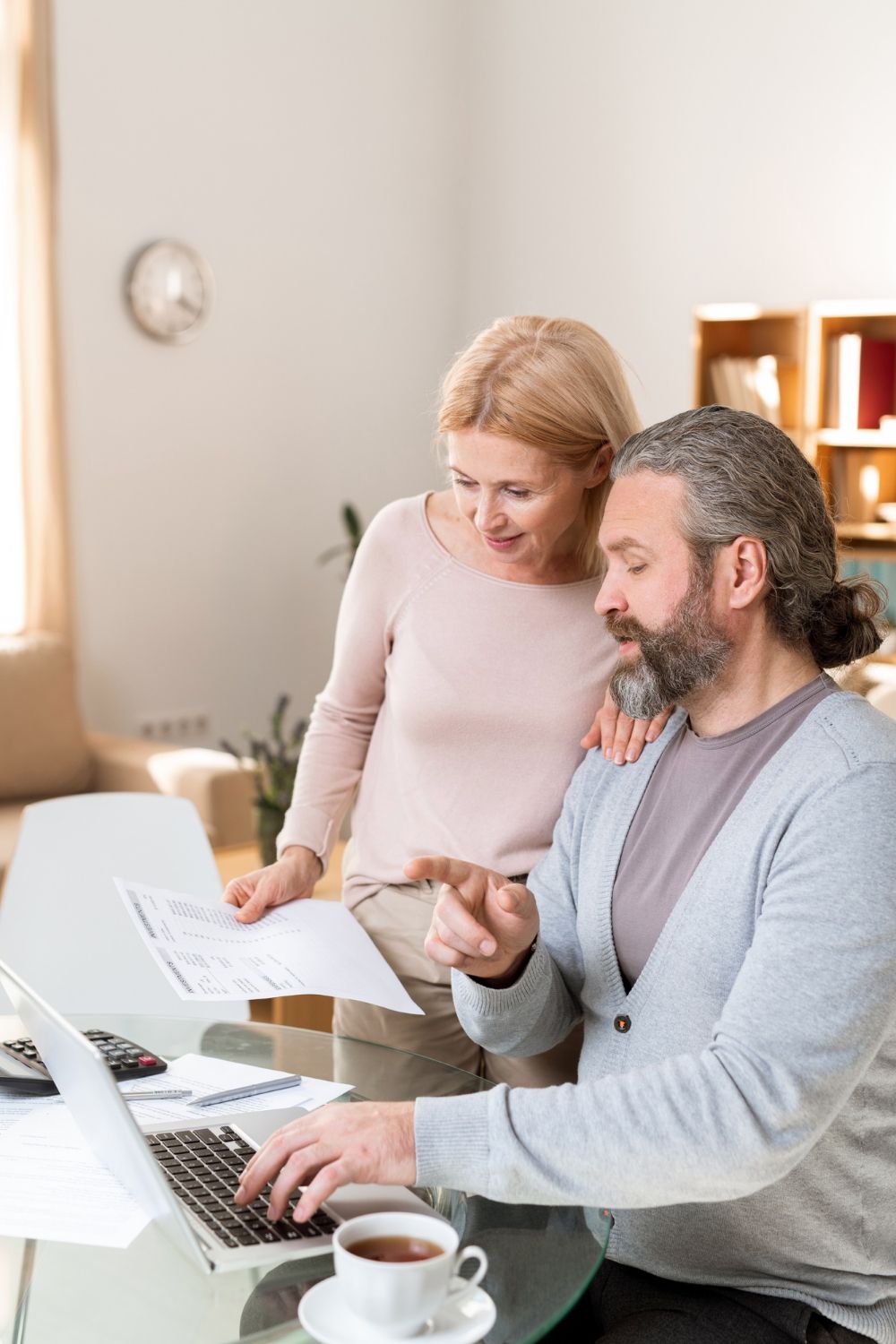 Woman and man reviewing documents at a laptop, with a cup of tea on a table.