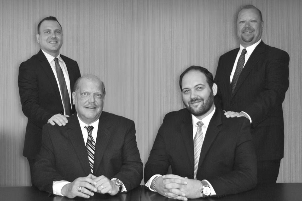 Four men in suits pose for a formal portrait.