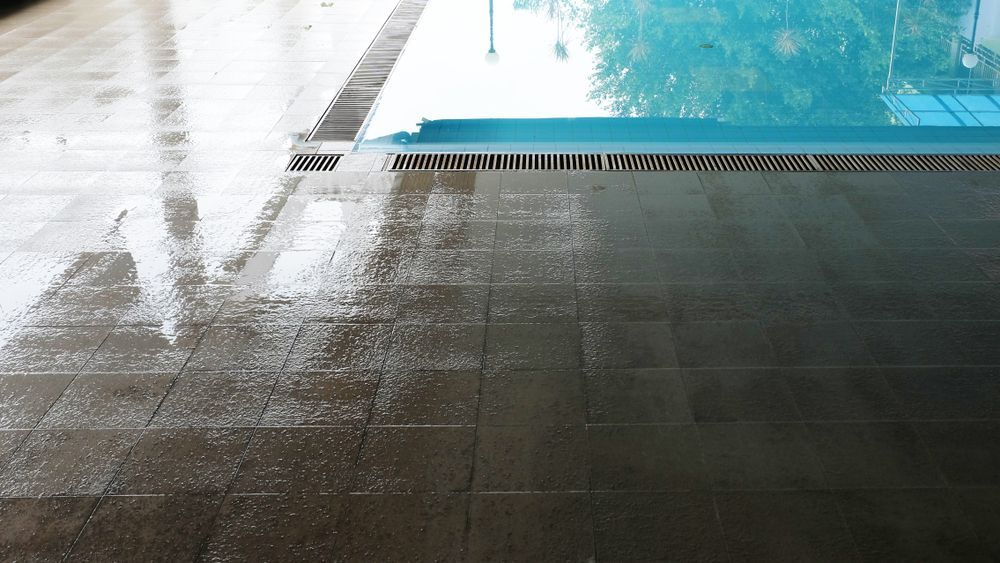 A Wet Tiled Floor Next to a Swimming Pool on a Rainy Day — The Tile & Stone Specialists in Maroochydore, QLD