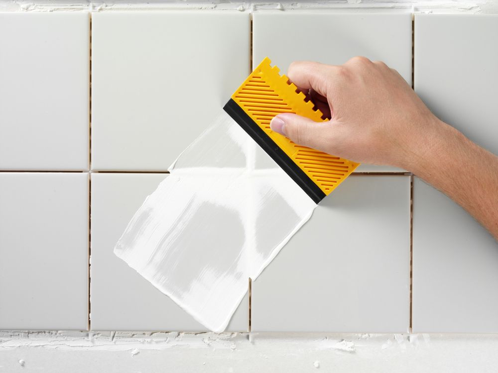 A Person is Cleaning a Tile Wall With a Spatula — The Tile & Stone Specialists in Nambour, QLD