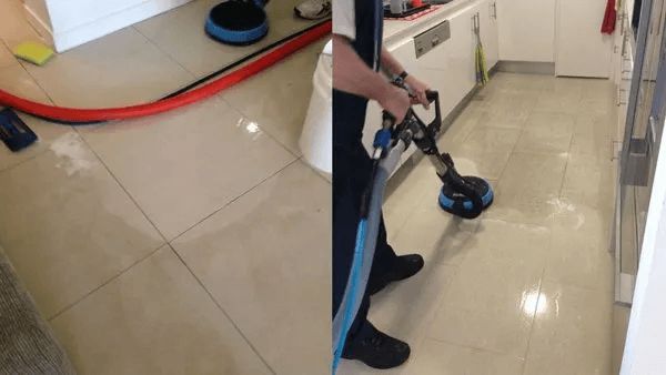 A Person is Cleaning a Tile Floor in a Kitchen With a Vacuum Cleaner — The Tile & Stone Specialists in Peregian Beach, QLD