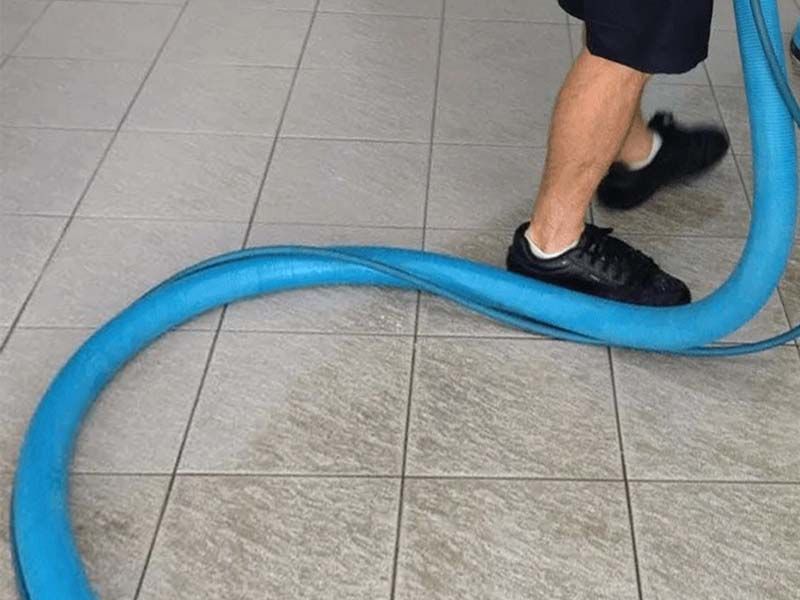 A Person is Using a Blue Hose to Clean a Tiled Floor — The Tile & Stone Specialists in Peregian Beach, QLD