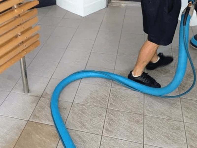 A Man is Using a Vacuum Cleaner on a Tiled Floor — The Tile & Stone Specialists in Peregian Beach, QLD