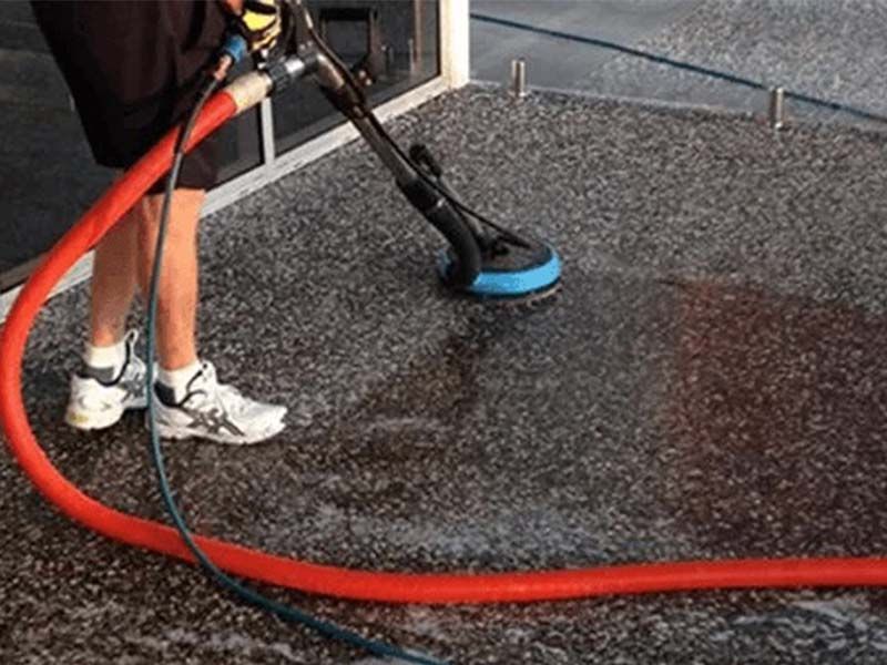 A Man is Cleaning a Concrete Floor With a Vacuum Cleaner — The Tile & Stone Specialists in Nambour, QLD