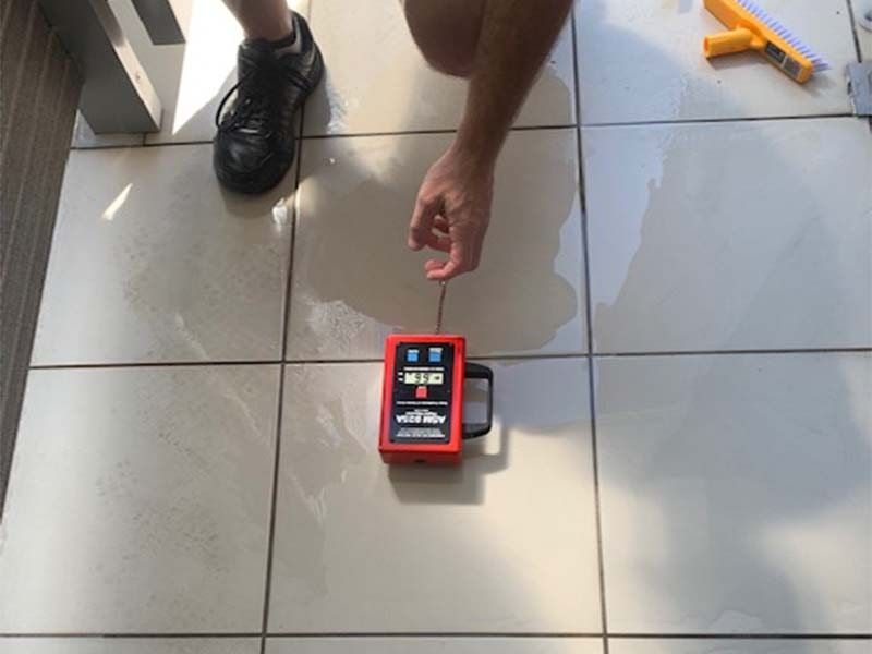 A Person is Using a Red Device on a Tiled Floor — The Tile & Stone Specialists in Peregian Beach, QLD