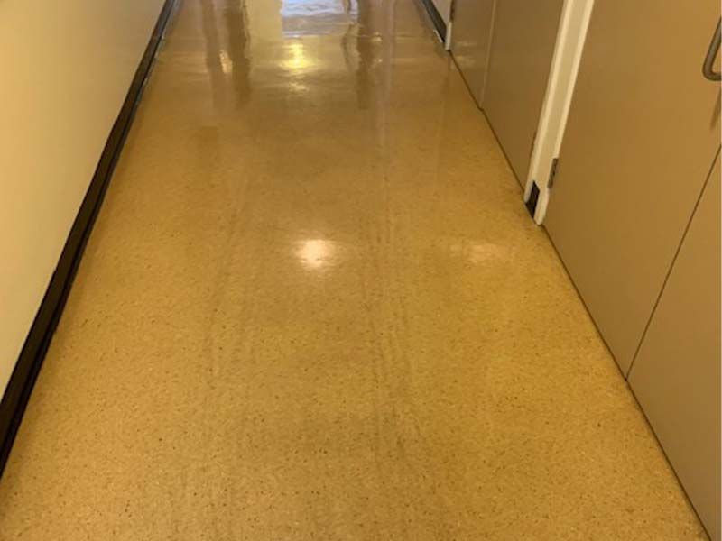 A Long Hallway With a Yellow Floor and a Few People Walking Down It — The Tile & Stone Specialists in Peregian Beach, QLD