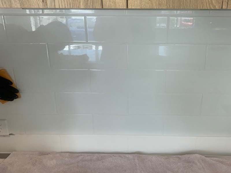 A Person is Cleaning a White Tile Wall With a Sponge — The Tile & Stone Specialists in Peregian Beach, QLD