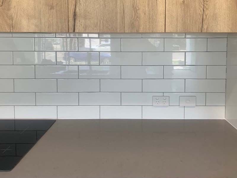 A Kitchen With White Tiles and Wooden Cabinets and a Stove Top Oven — The Tile & Stone Specialists in Peregian Beach, QLD