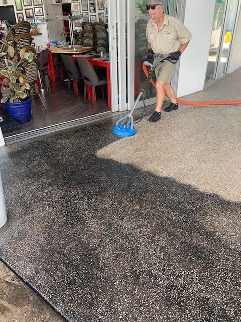 A Man is Cleaning a Concrete Floor With a Vacuum Cleaner — The Tile & Stone Specialists in Peregian Beach, QLD