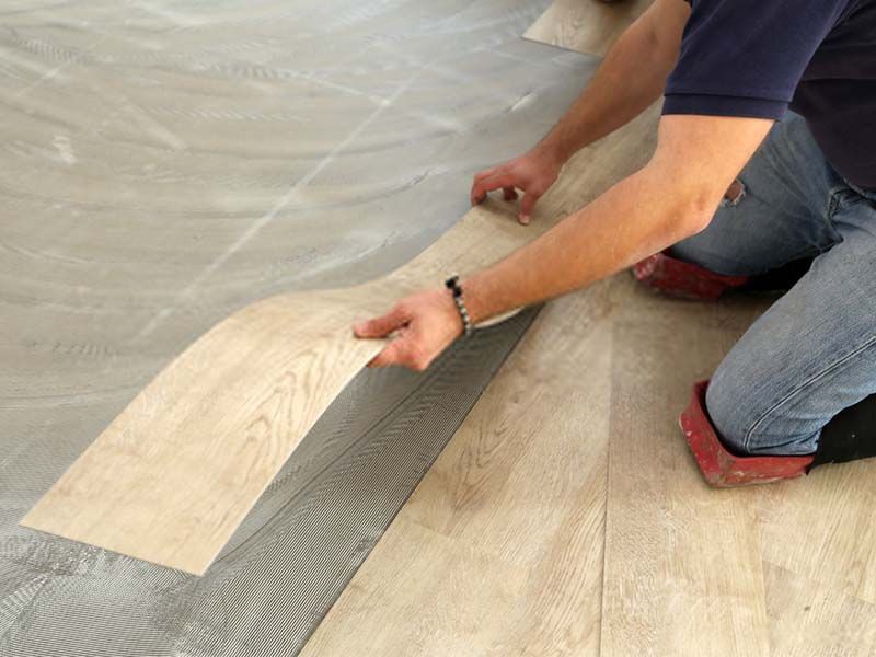 A Man is Kneeling on the Floor Holding a Piece of Wood — The Tile & Stone Specialists in Peregian Beach, QLD