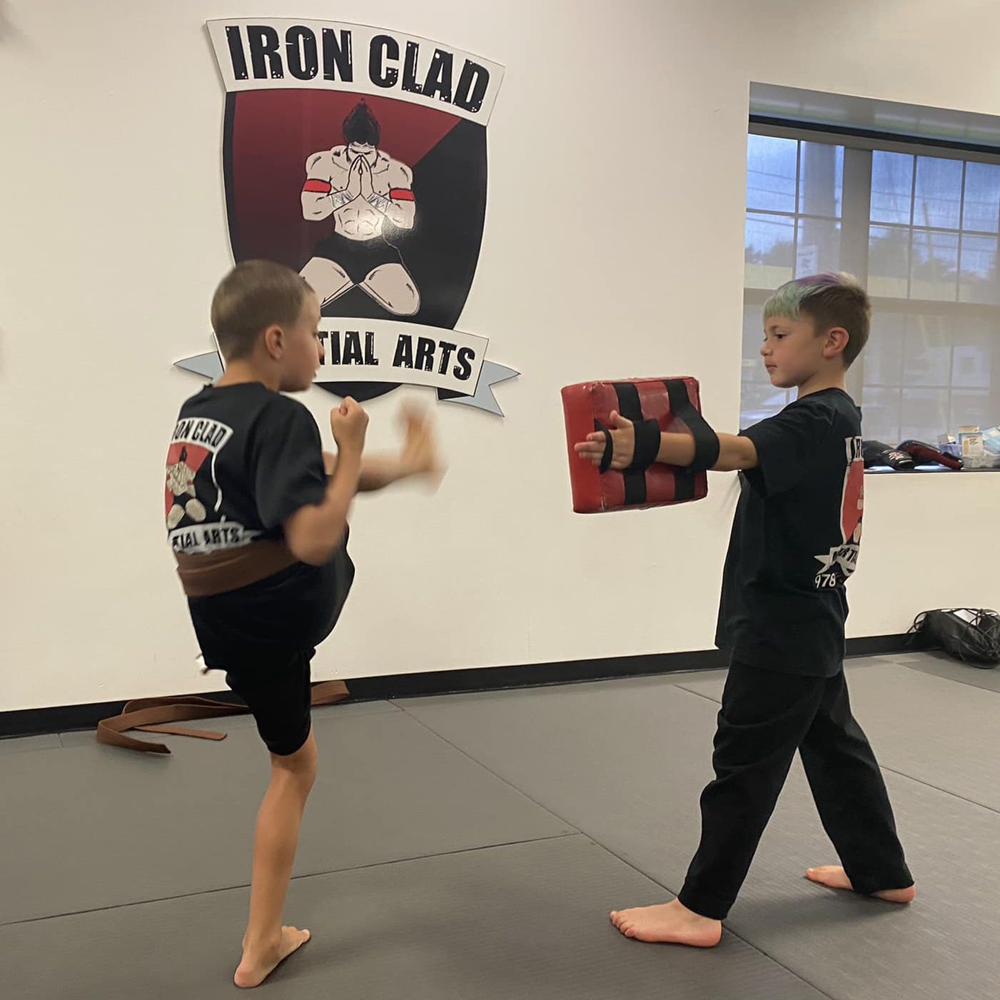 Two young boys are practicing martial arts in front of a sign that says iron clad