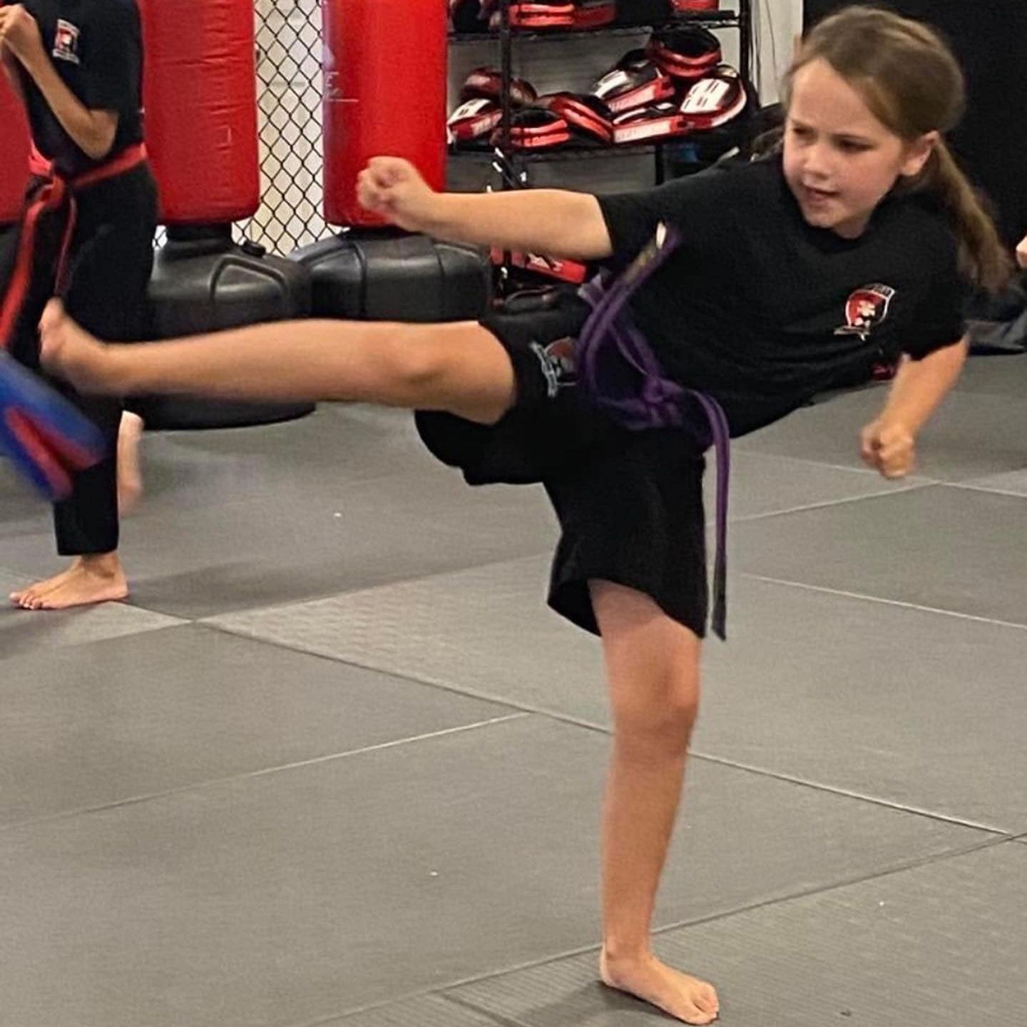 A young girl is kicking a ball in a gym