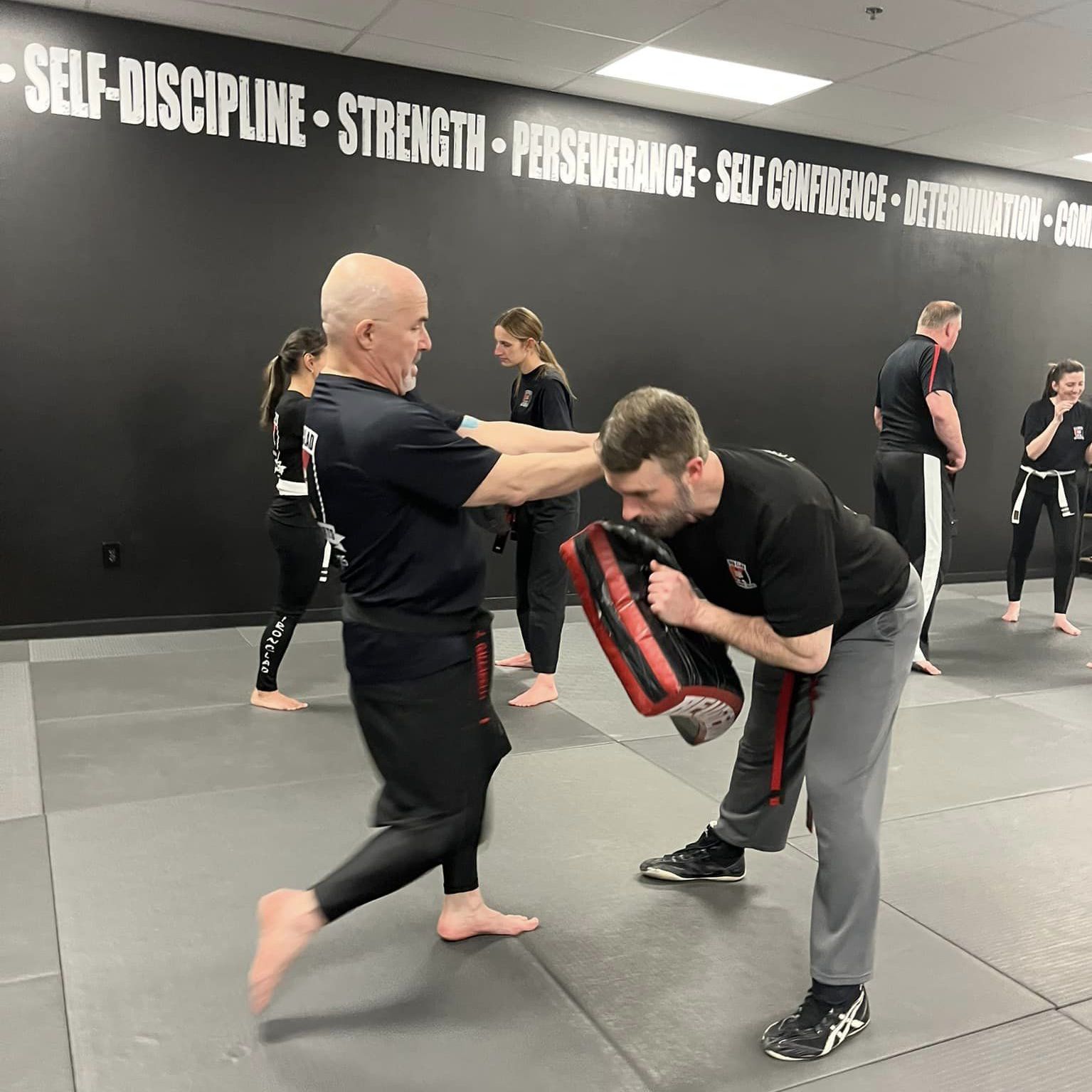 A group of people are practicing martial arts in front of a wall that says self discipline strength perseverance self confidence