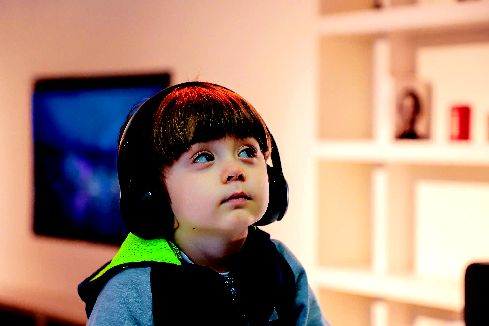 A young boy wearing headphones is looking up in a living room.