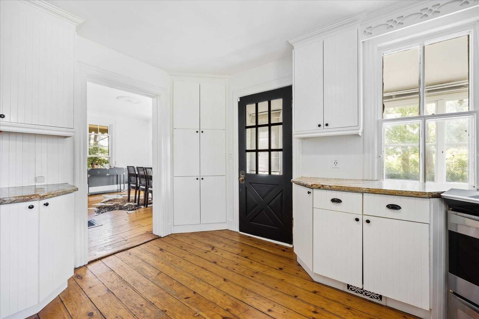 A kitchen with white cabinets and wooden floors and a black door.